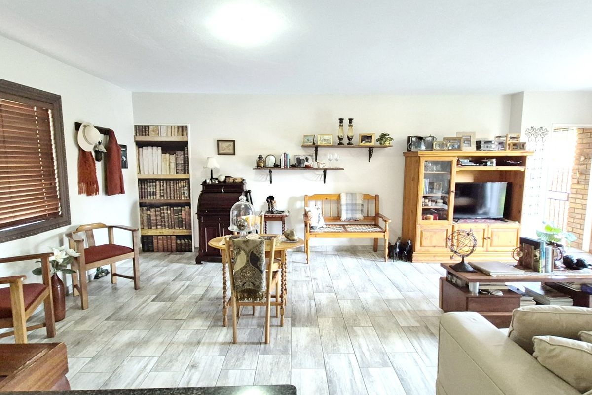 Spacious living room featuring modern wood-look tiled flooring, built-in shelving, and natural light through timber-blinded windows.