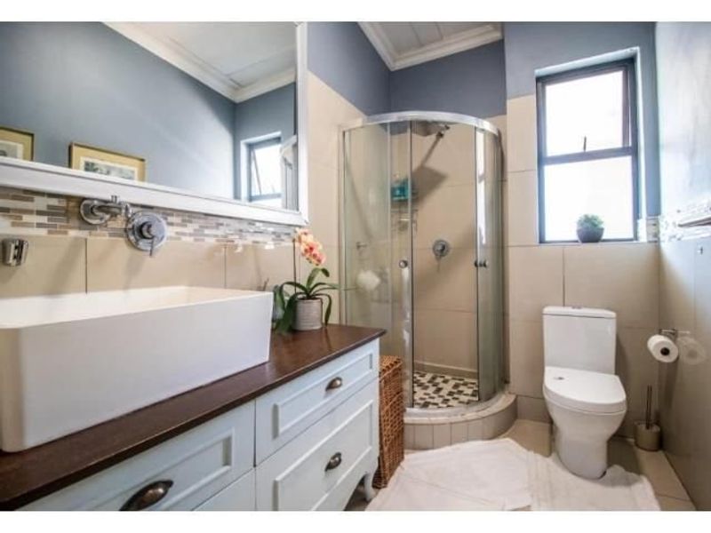 A well-maintained bathroom featuring a modern vanity with a vessel sink, a corner shower enclosure, and neutral wall tiling.