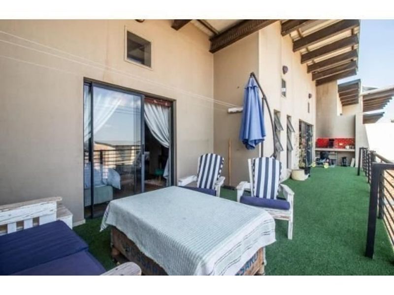 Spacious covered balcony featuring artificial turf, a built-in braai area, and sliding door access to the interior living space.