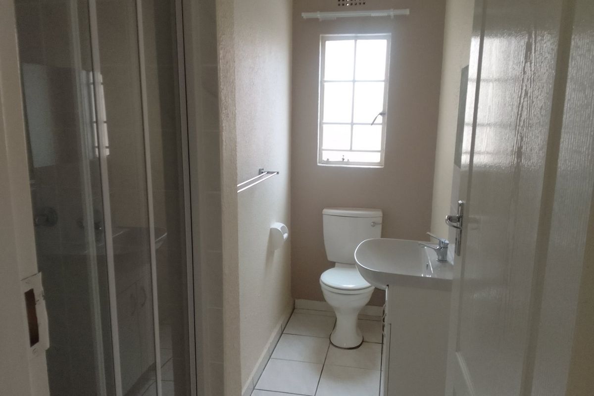 A compact bathroom featuring a shower enclosure, pedestal washbasin, and toilet with tiled flooring and natural light from a window.