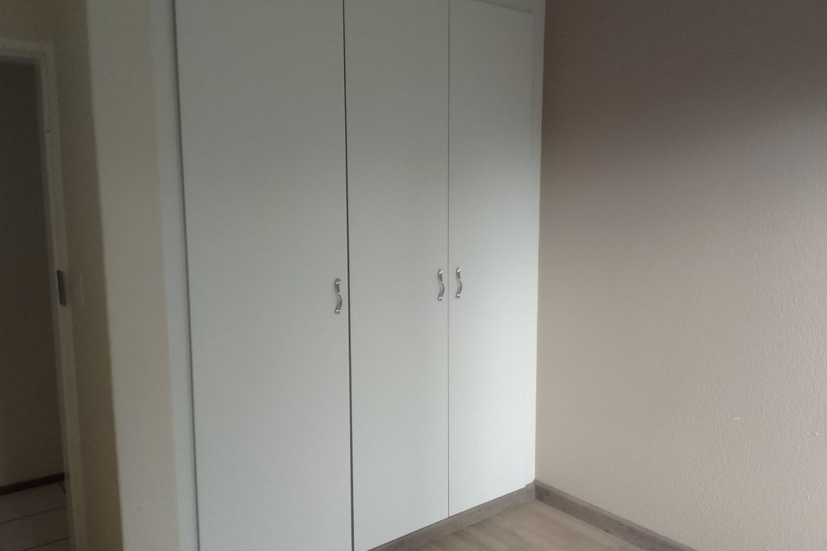 A clean, empty bedroom featuring neutral walls, modern laminate flooring, and a functional built-in wardrobe with white doors.