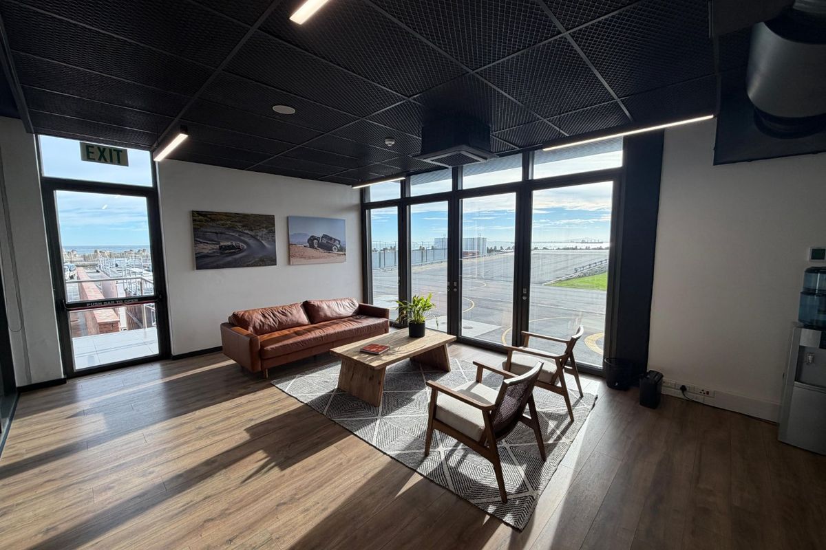 Modern commercial lounge area featuring high-contrast black grid ceilings, linear lighting, and expansive floor-to-ceiling windows with scenic exterior views.