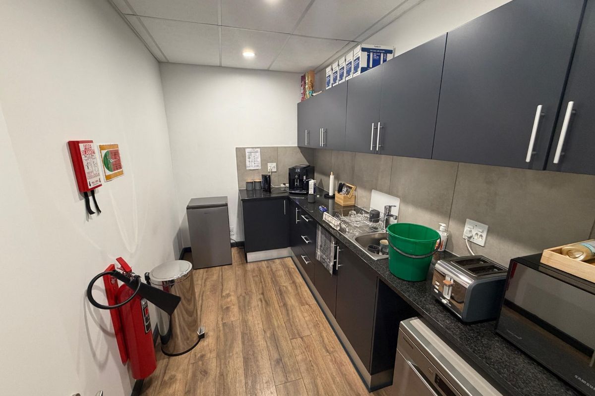 A functional commercial kitchenette featuring dark cabinetry, laminate countertops, a stainless steel sink, and essential safety equipment including a fire extinguisher and blanket.