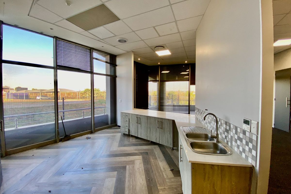 Modern commercial kitchenette featuring built-in cabinetry, double sink, herringbone-patterned flooring, and expansive floor-to-ceiling windows providing ample natural light.