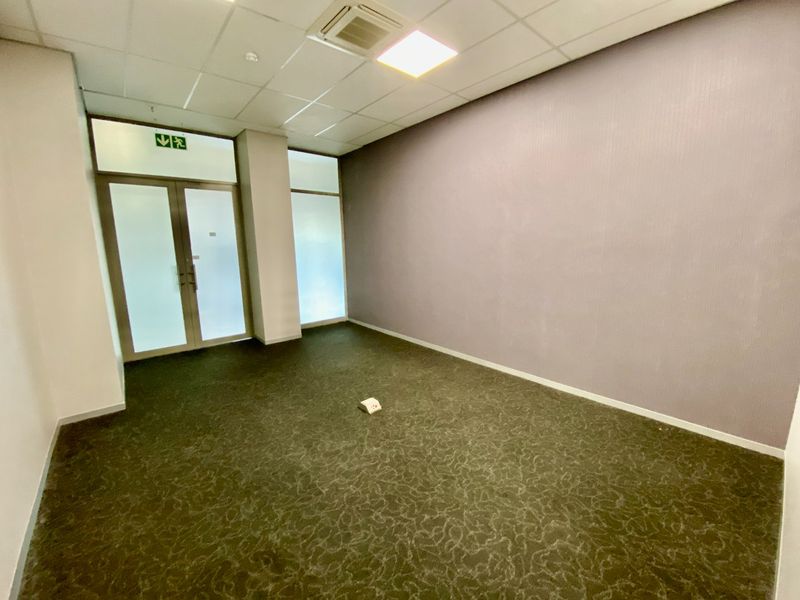 A vacant commercial office space featuring carpeted flooring, a suspended ceiling with recessed lighting, and a glass-panelled entrance door.