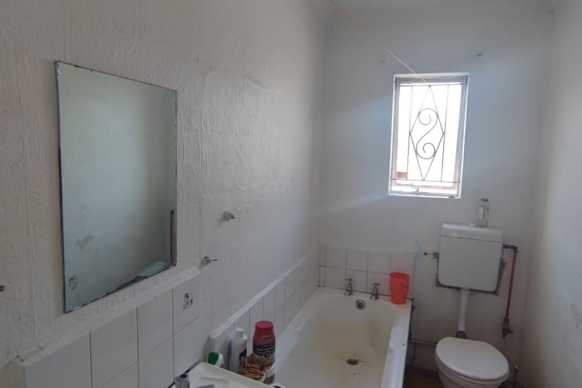 A compact bathroom featuring a bathtub, toilet, and security-barred window, requiring cosmetic updates and maintenance to improve its overall condition.