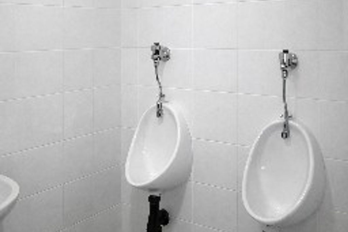 A clean commercial restroom facility featuring two wall-mounted ceramic urinals with exposed plumbing and neutral tiled finishes.