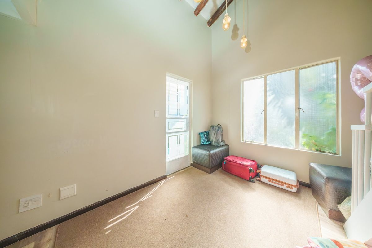 A bright living area featuring high ceilings with exposed timber beams, large windows for natural light, and direct access to the exterior.