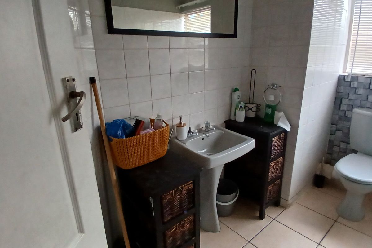 A functional bathroom featuring a pedestal basin, standard toilet, and tiled finishes, offering potential for modernization and cosmetic updates.