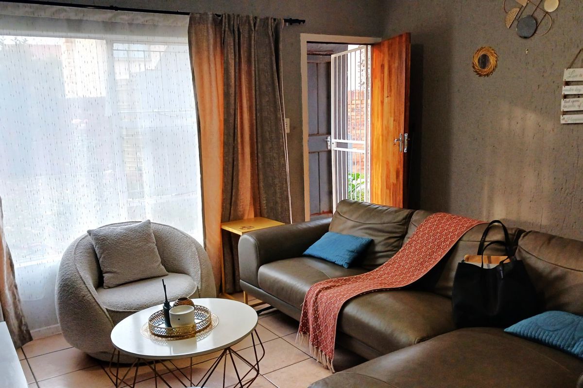 A cozy living room featuring tiled flooring, a large window with curtains, and a wooden door leading to an exterior security gate.