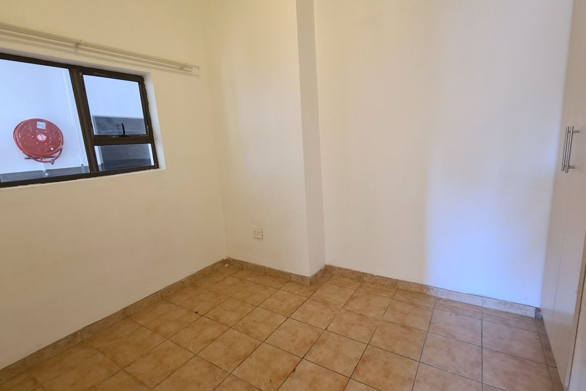 A compact, empty bedroom featuring tiled flooring, a built-in cupboard, and a window with an exterior view.