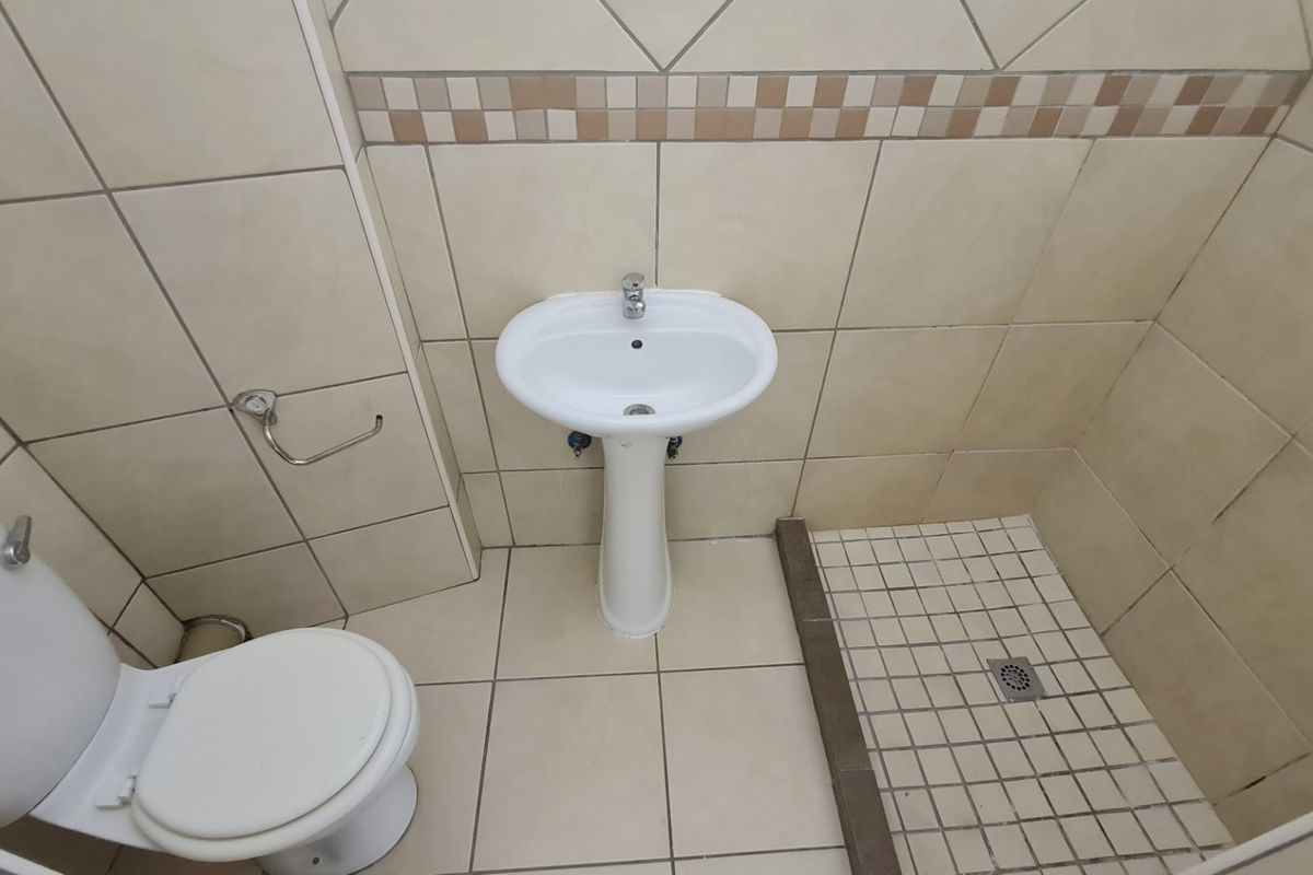 A functional bathroom featuring a pedestal basin, toilet, and a tiled shower area with neutral ceramic finishes.