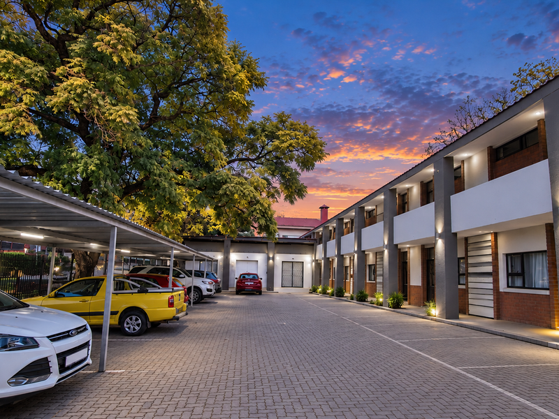 A well-maintained commercial property exterior featuring a paved parking area with covered bays and modern brick and plaster facade detailing.
