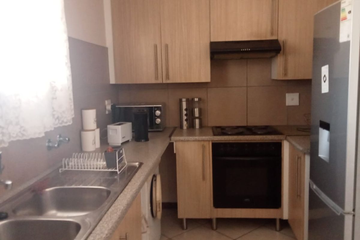 A functional kitchen featuring light wood-finish cabinetry, a double bowl sink, built-in oven, hob, and extractor fan with tiled backsplash.