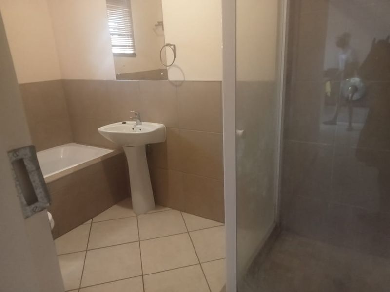 A functional bathroom featuring a pedestal basin, built-in bathtub, and a separate shower enclosure with neutral wall and floor tiling.