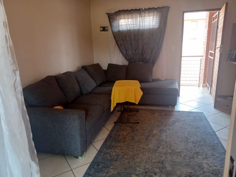 A living room area featuring tiled flooring and direct access to an external balcony through a security gate.