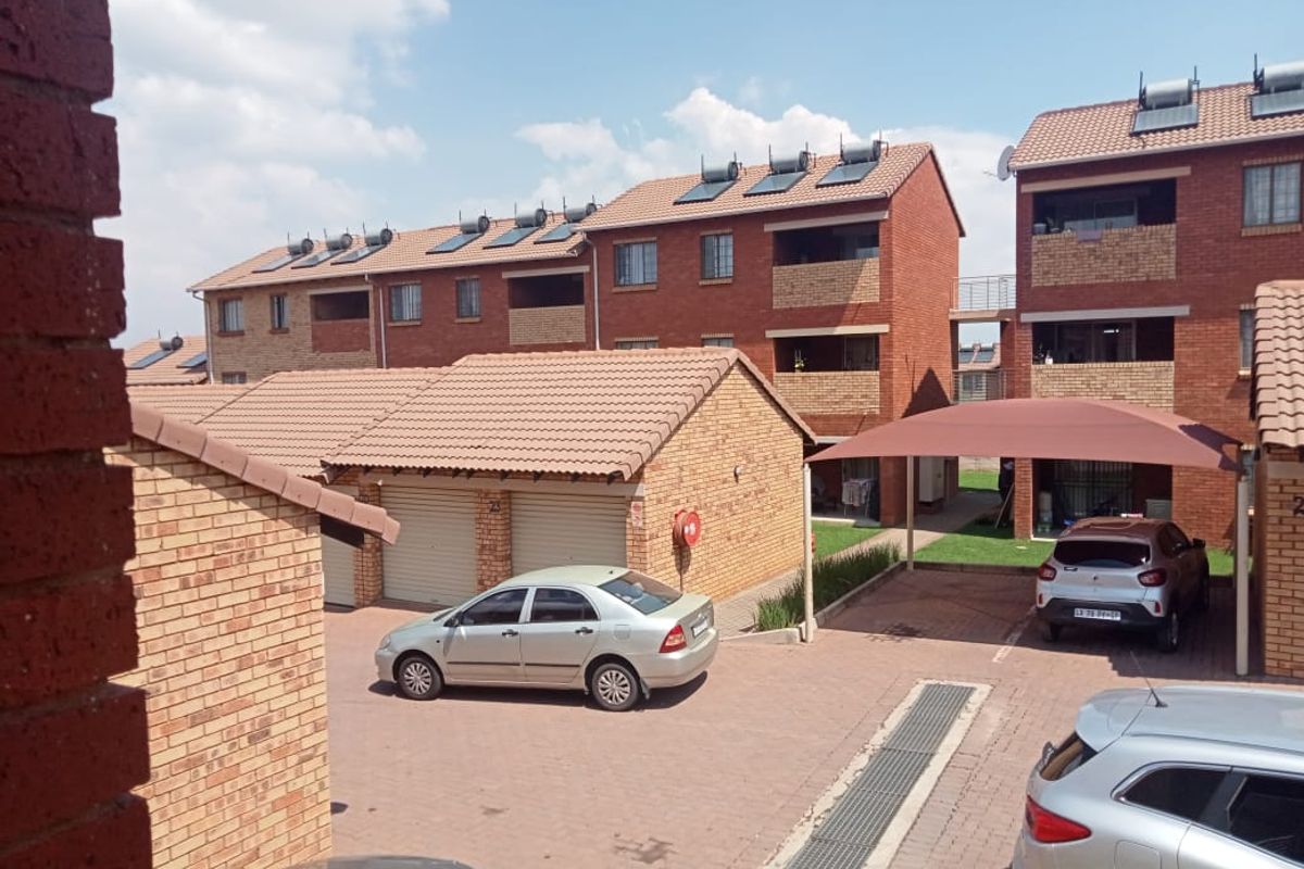 Exterior view of a residential apartment complex featuring face brick buildings, tiled roofs with solar panels, paved parking areas, and covered carports.