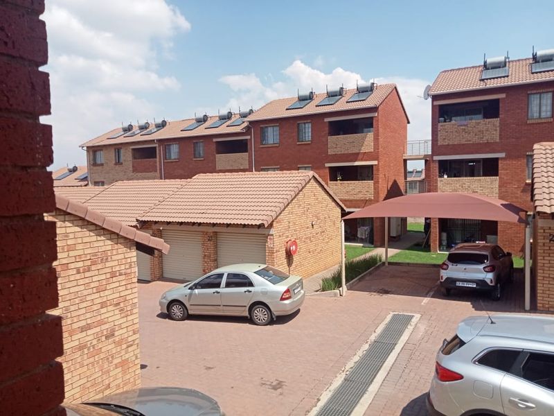 Exterior view of a residential apartment complex featuring face brick buildings, tiled roofs with solar panels, paved parking areas, and covered carports.