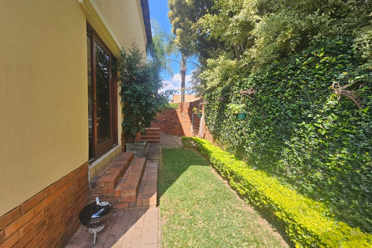 A private rear garden featuring a manicured lawn, established hedge, brick boundary wall, and paved patio area with direct access to the home.