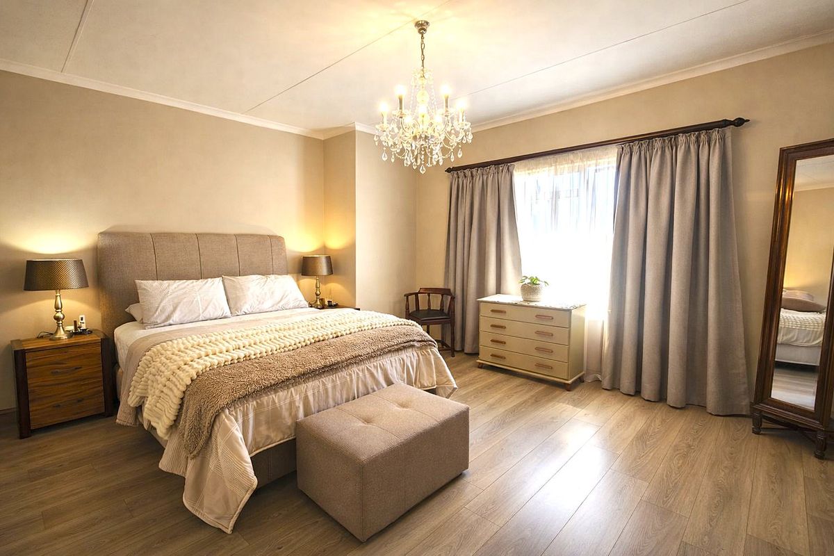 A well-maintained bedroom featuring light-toned laminate flooring, neutral wall finishes, and an elegant crystal chandelier.