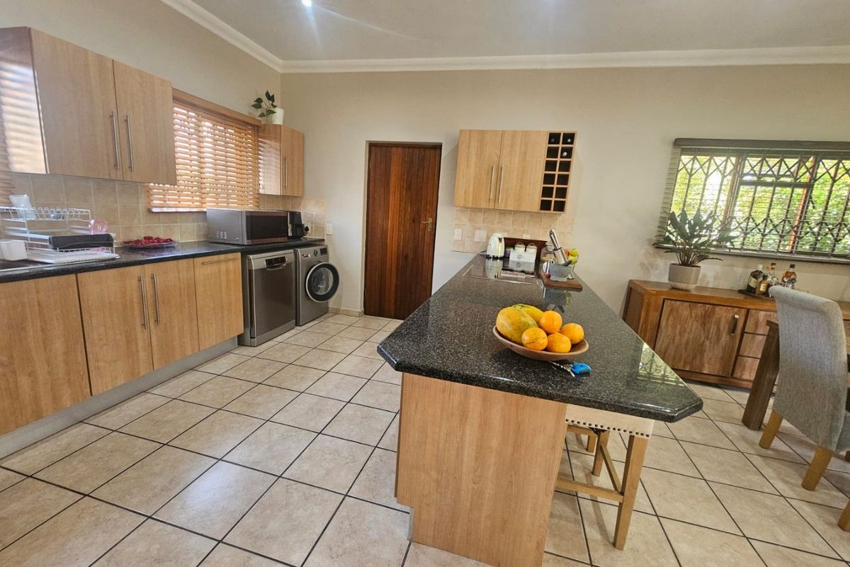 A functional kitchen featuring light wood cabinetry, granite countertops, a central island, and ceramic floor tiles with integrated appliance spaces.