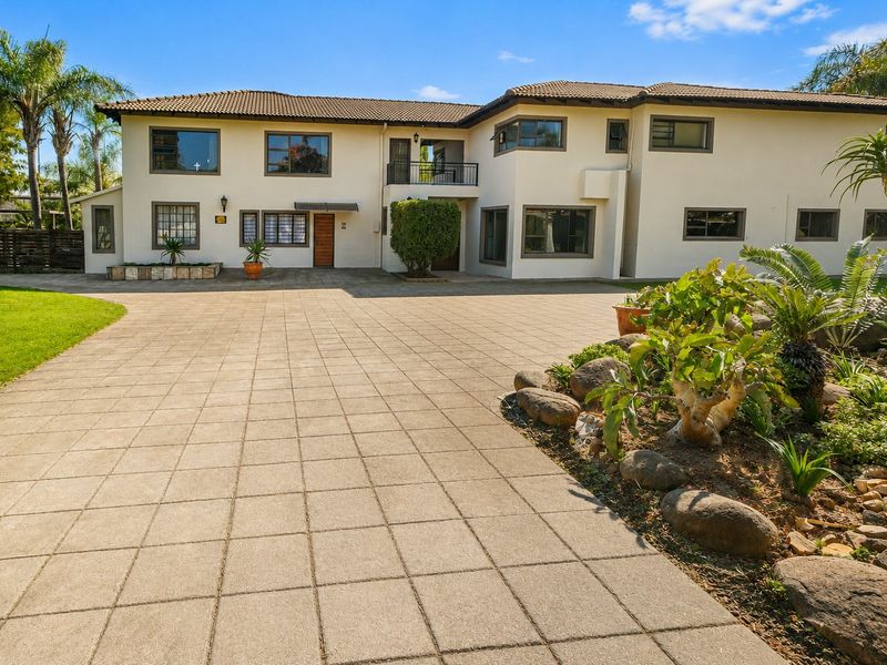 Spacious front exterior view of a two-story house featuring a large paved driveway, landscaped garden, and a balcony.