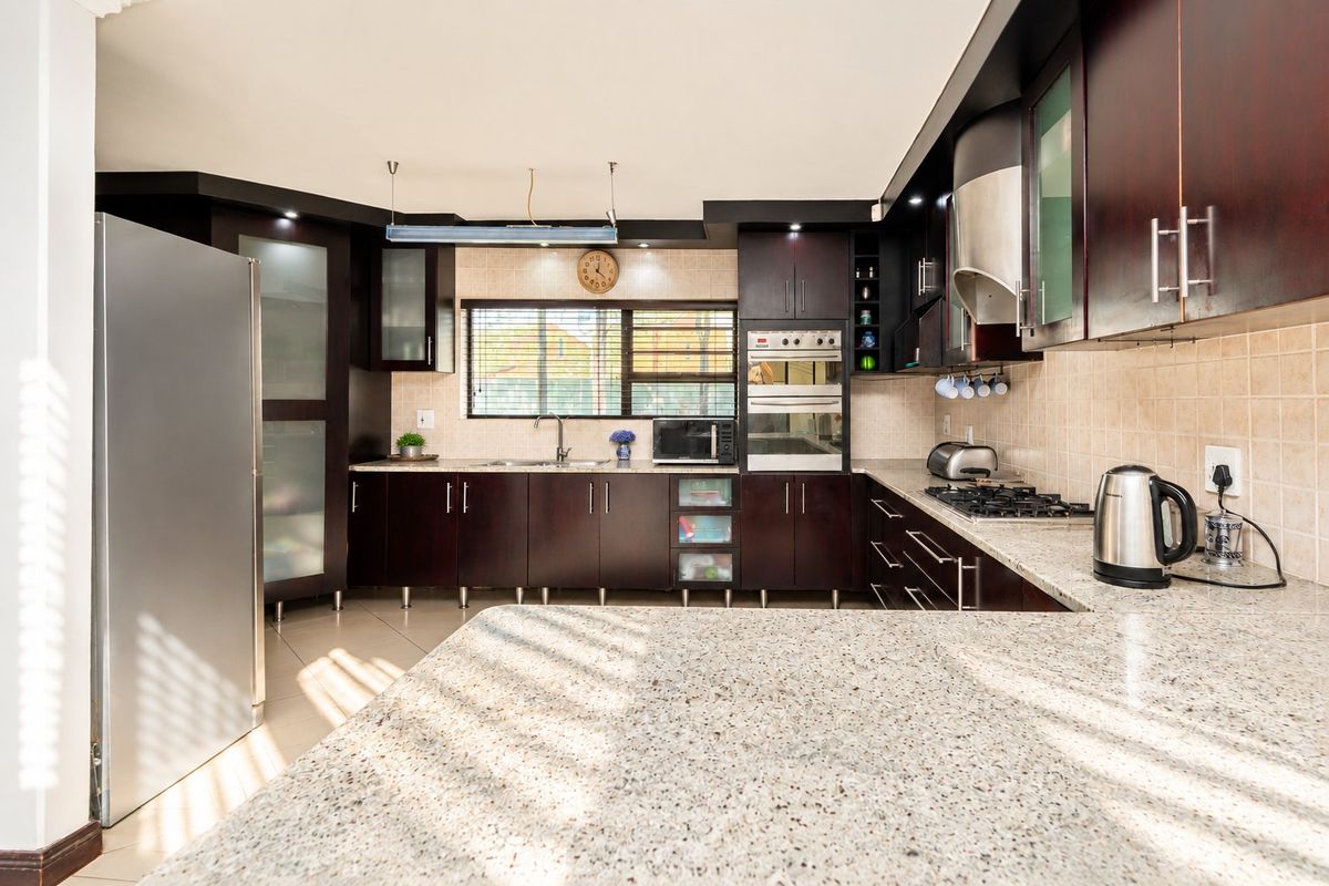 A well-appointed kitchen featuring dark wood cabinetry, granite countertops, a built-in oven, gas hob, and a tiled backsplash with ample workspace.