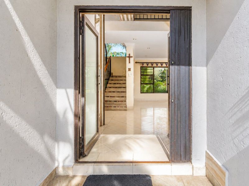 A bright and welcoming entrance area featuring tiled flooring and a staircase leading to the upper level, viewed from the exterior threshold.
