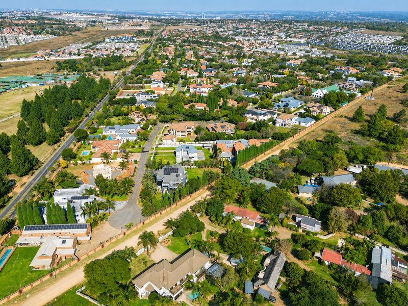 An elevated aerial view of a suburban residential estate featuring established homes, landscaped gardens, swimming pools, and surrounding infrastructure.