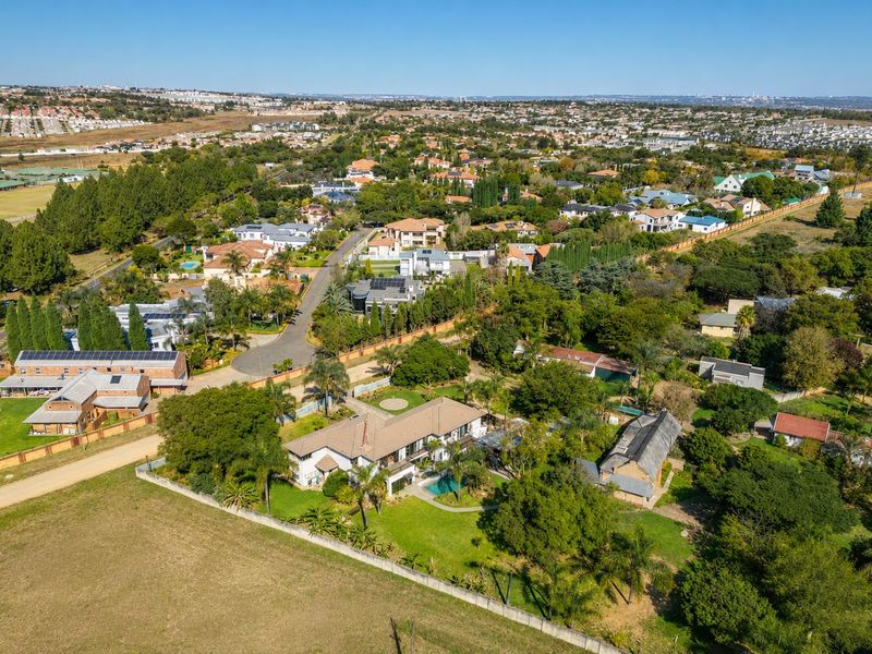 An aerial view of the property showcasing the expansive garden, swimming pool, and surrounding residential estate landscape.