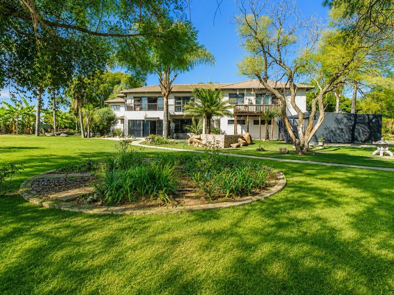 Spacious rear garden featuring a well-maintained lawn, mature trees, circular garden bed, and a multi-level residential facade with balcony and terrace access.