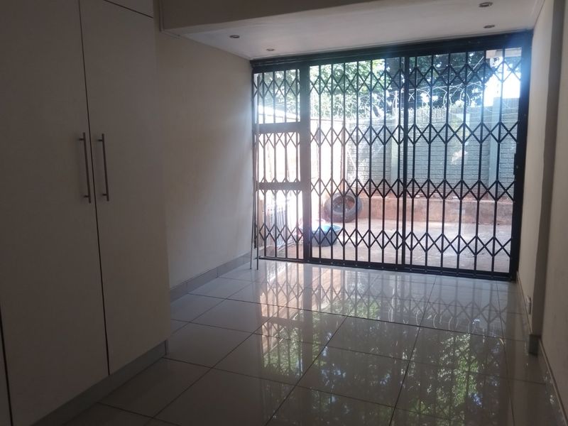 An empty living area featuring tiled flooring, built-in cupboards, and a sliding door with a security gate leading to the exterior.