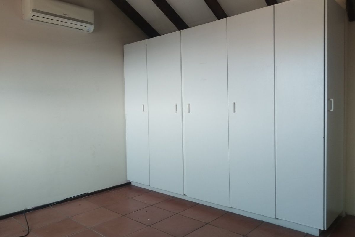 An empty bedroom featuring built-in white cupboards, exposed timber ceiling beams, tiled flooring, and a wall-mounted split-system air conditioning unit.