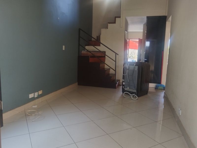 An open-plan living area featuring tiled flooring and a central staircase with a metal handrail, presenting a blank canvas for interior design.