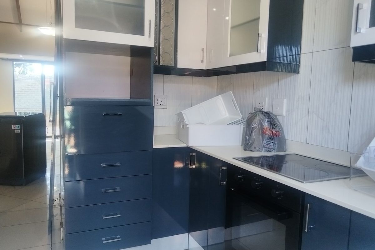 A modern kitchen featuring high-gloss dark blue and white cabinetry, a built-in oven, electric hob, and tiled backsplash.