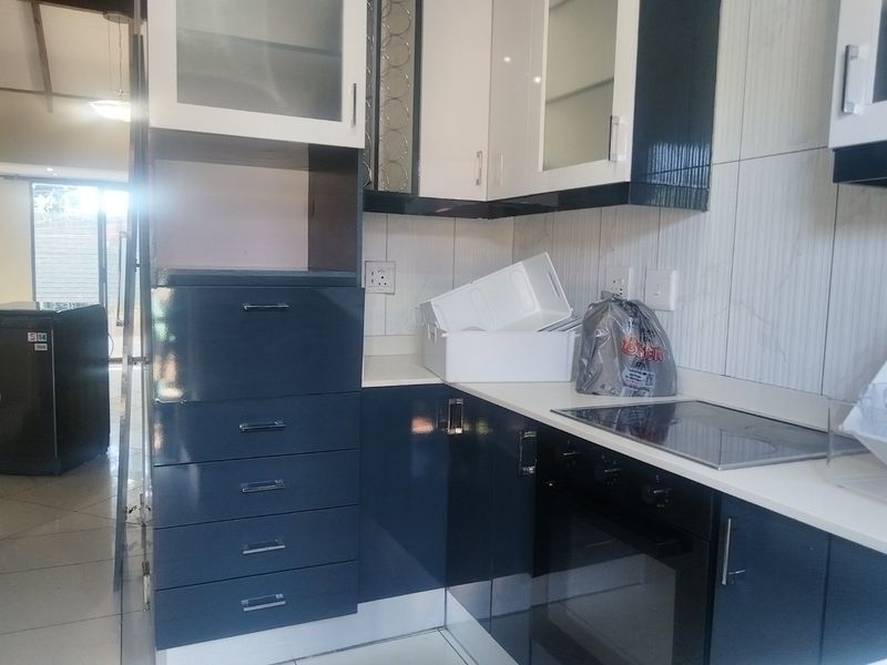A modern kitchen featuring high-gloss dark blue and white cabinetry, a built-in oven, electric hob, and tiled backsplash.