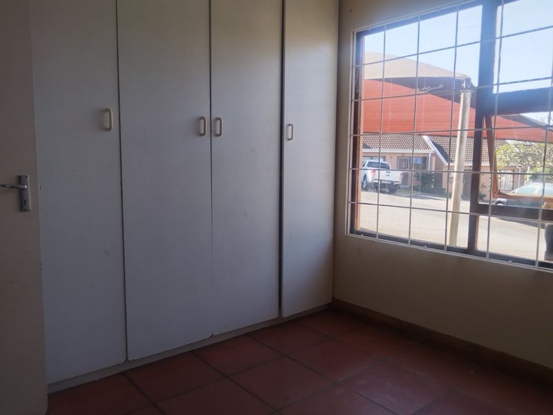 A vacant bedroom featuring built-in cupboards, tiled flooring, and a window fitted with security bars.