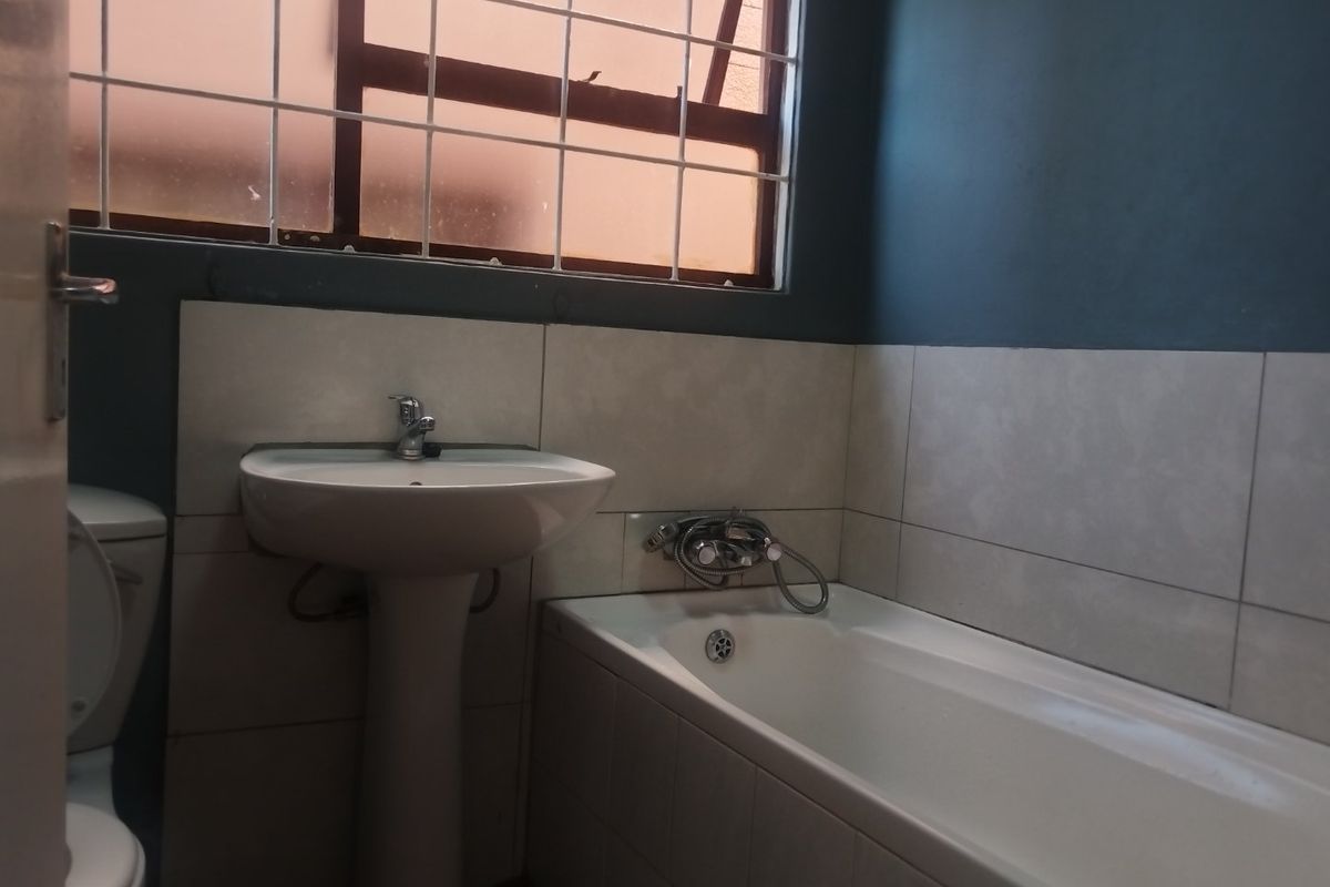 A functional bathroom featuring a pedestal washbasin, bathtub with chrome fixtures, and tiled walls, providing a clean and practical space.