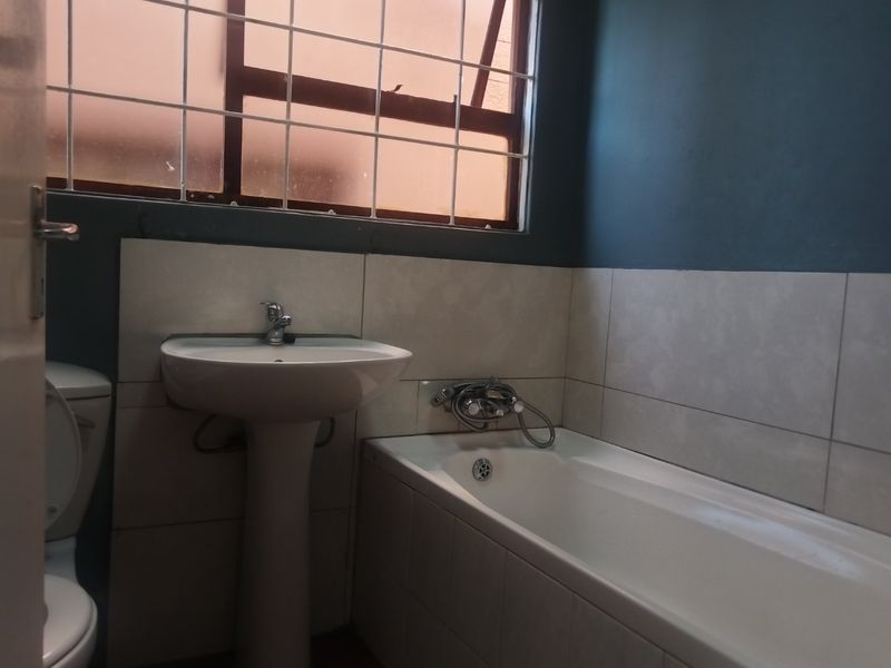 A functional bathroom featuring a pedestal washbasin, bathtub with chrome fixtures, and tiled walls, providing a clean and practical space.