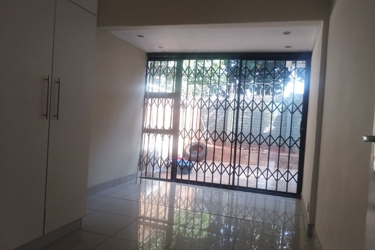 An empty living area featuring tiled flooring, built-in cupboards, and a sliding glass door with a security gate leading to the exterior.