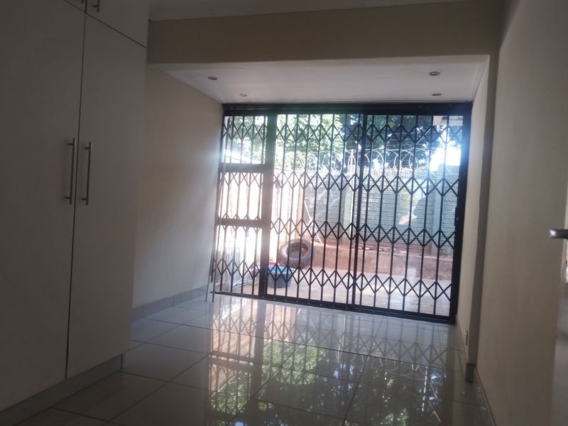 An empty living area featuring tiled flooring, built-in cupboards, and a sliding glass door with a security gate leading to the exterior.