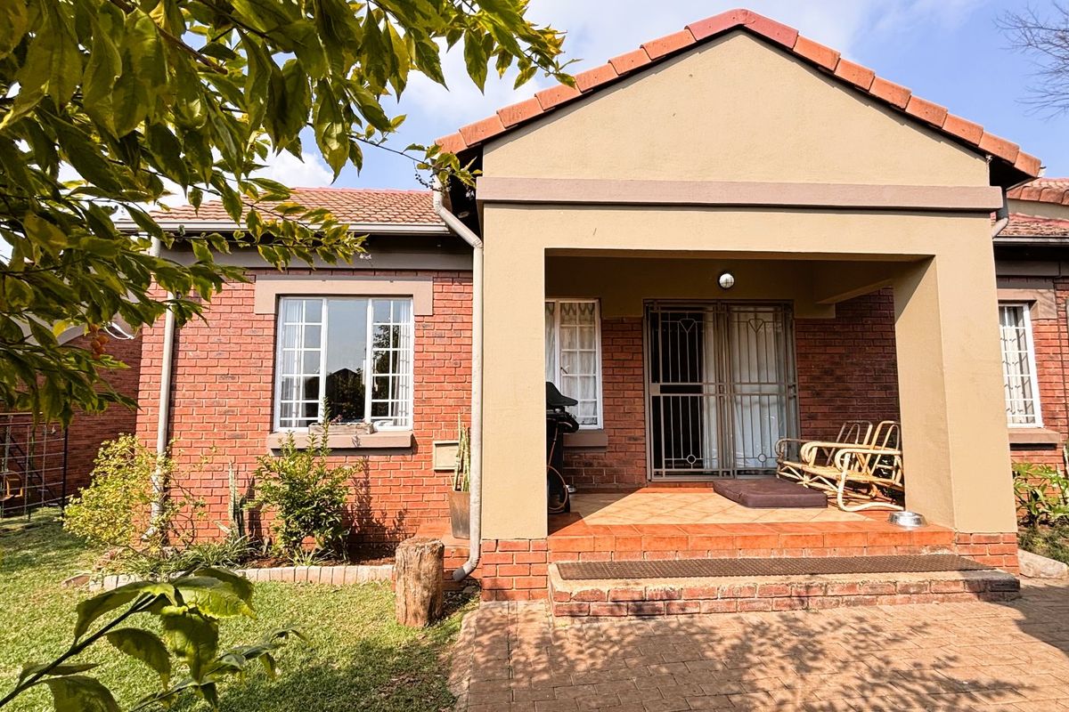 A well-maintained rear exterior view of the townhouse featuring a covered patio, facebrick facade, and terracotta roof tiles overlooking a private garden area.