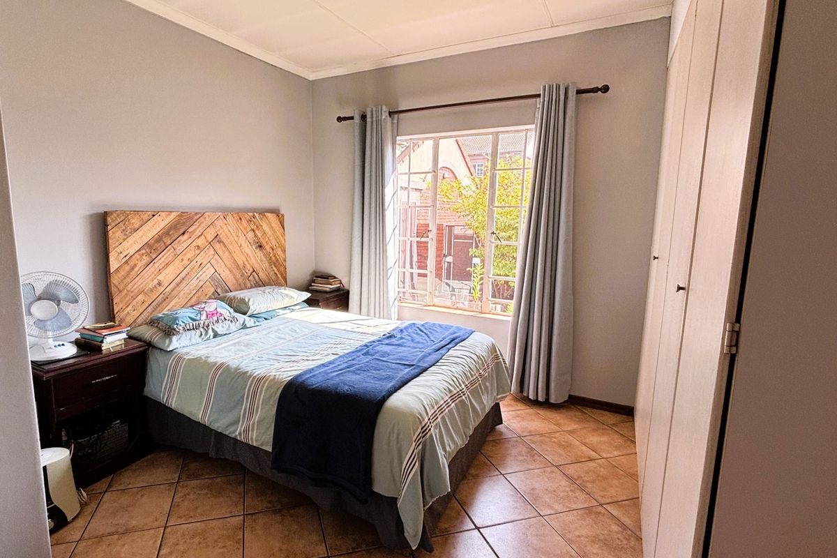 A bedroom featuring tiled flooring, built-in cupboards, and a window with security bars, providing a functional and well-lit living space.