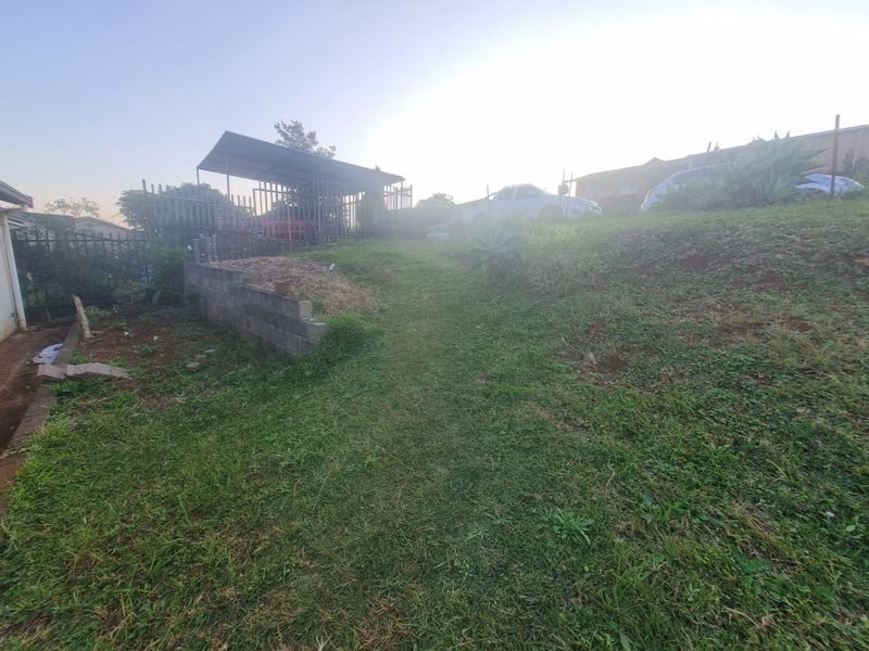 A sloped garden area featuring a retaining wall, metal carport structure, and perimeter fencing, requiring landscaping and maintenance to improve curb appeal.