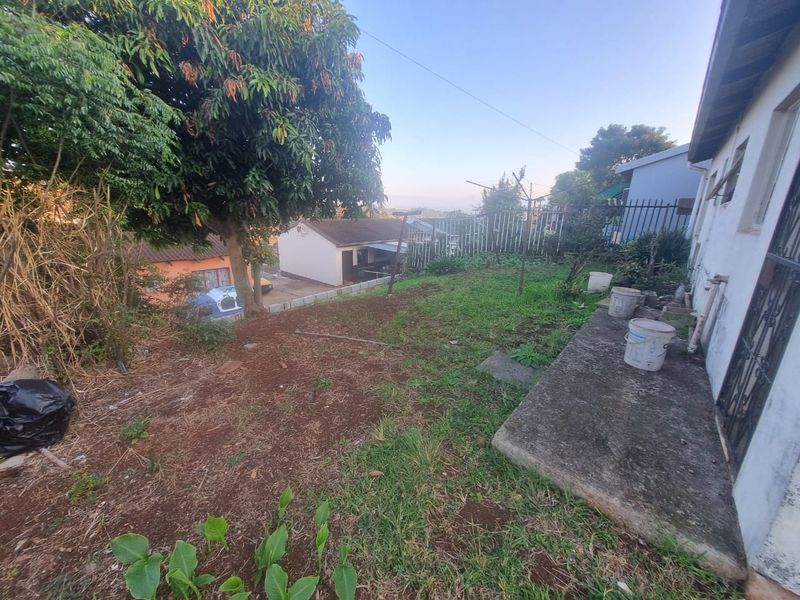 A rear garden area featuring a concrete pathway, mature trees, and views of the surrounding property, offering potential for landscaping and outdoor improvement.