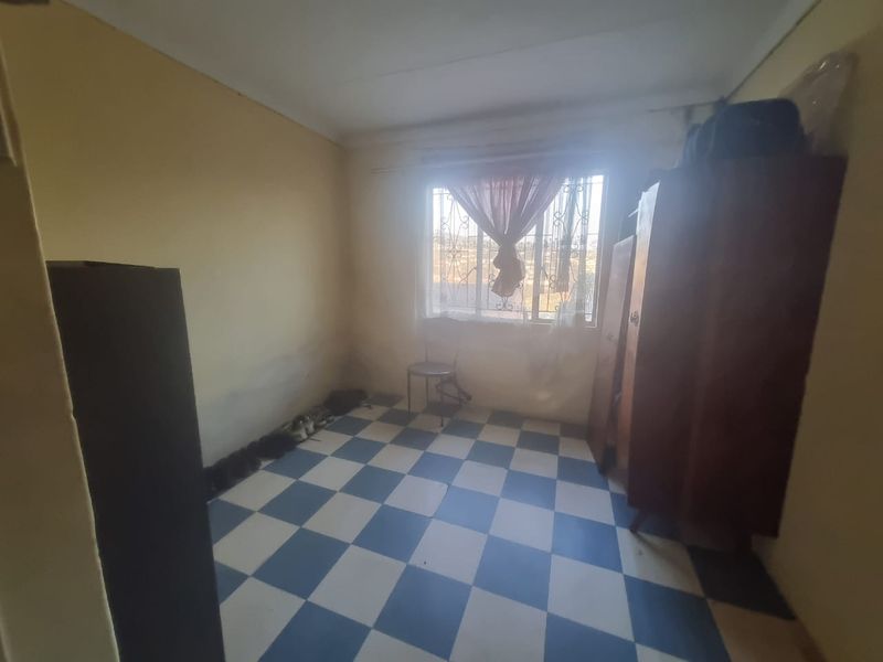 A bedroom featuring checkered floor tiles and security bars on the window, requiring cosmetic updates to improve its overall condition.