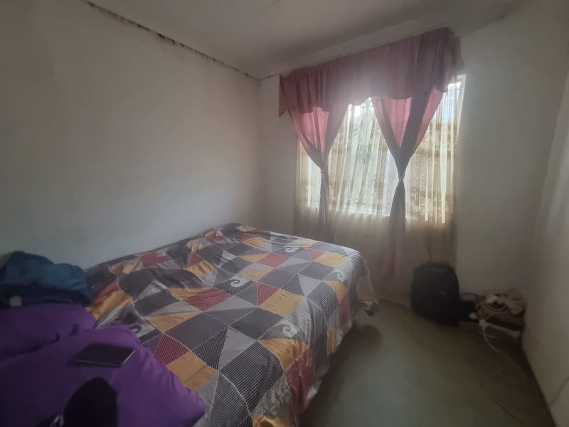 A bedroom featuring a window with security bars, showing signs of ceiling water damage and requiring maintenance to the wall and ceiling finishes.