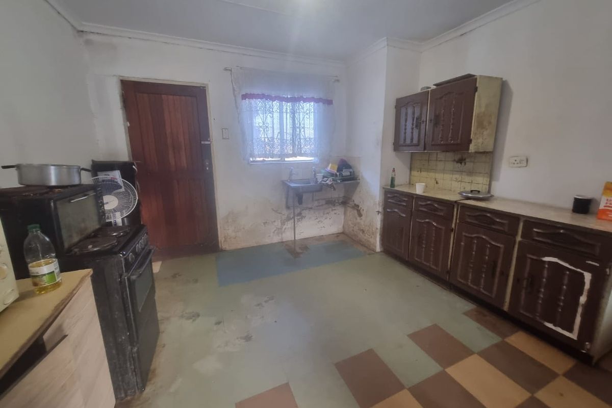 A dated kitchen featuring original cabinetry, a stainless steel sink, and tiled backsplash, requiring significant renovation and cosmetic updates to improve functionality and aesthetic appeal.