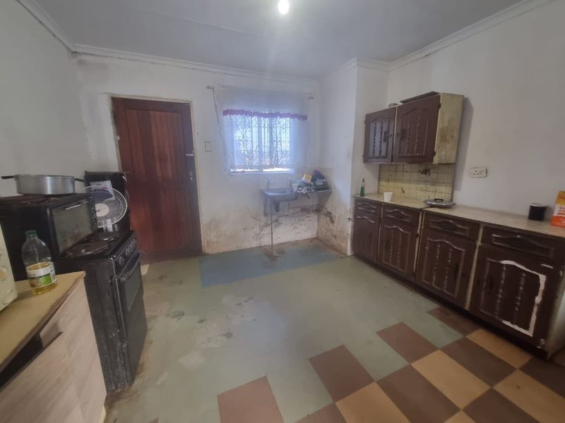 A dated kitchen featuring original cabinetry, a stainless steel sink, and tiled backsplash, requiring significant renovation and cosmetic updates to improve functionality and aesthetic appeal.