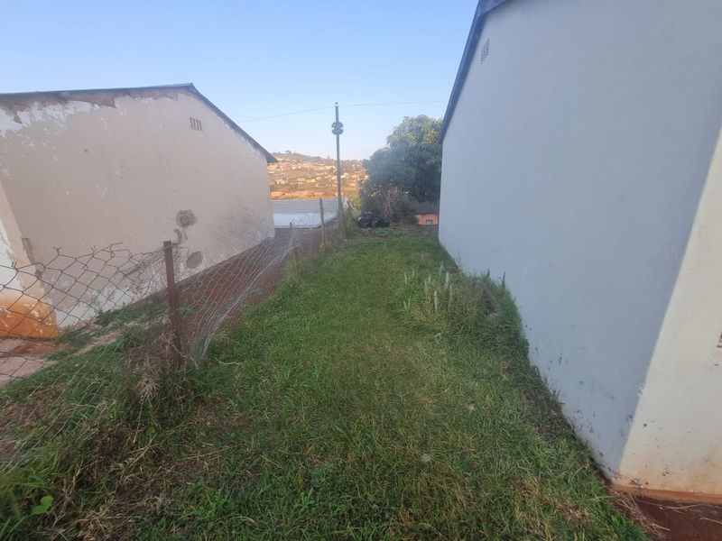 A narrow side passage between two residential structures featuring a grass lawn and wire mesh boundary fencing.